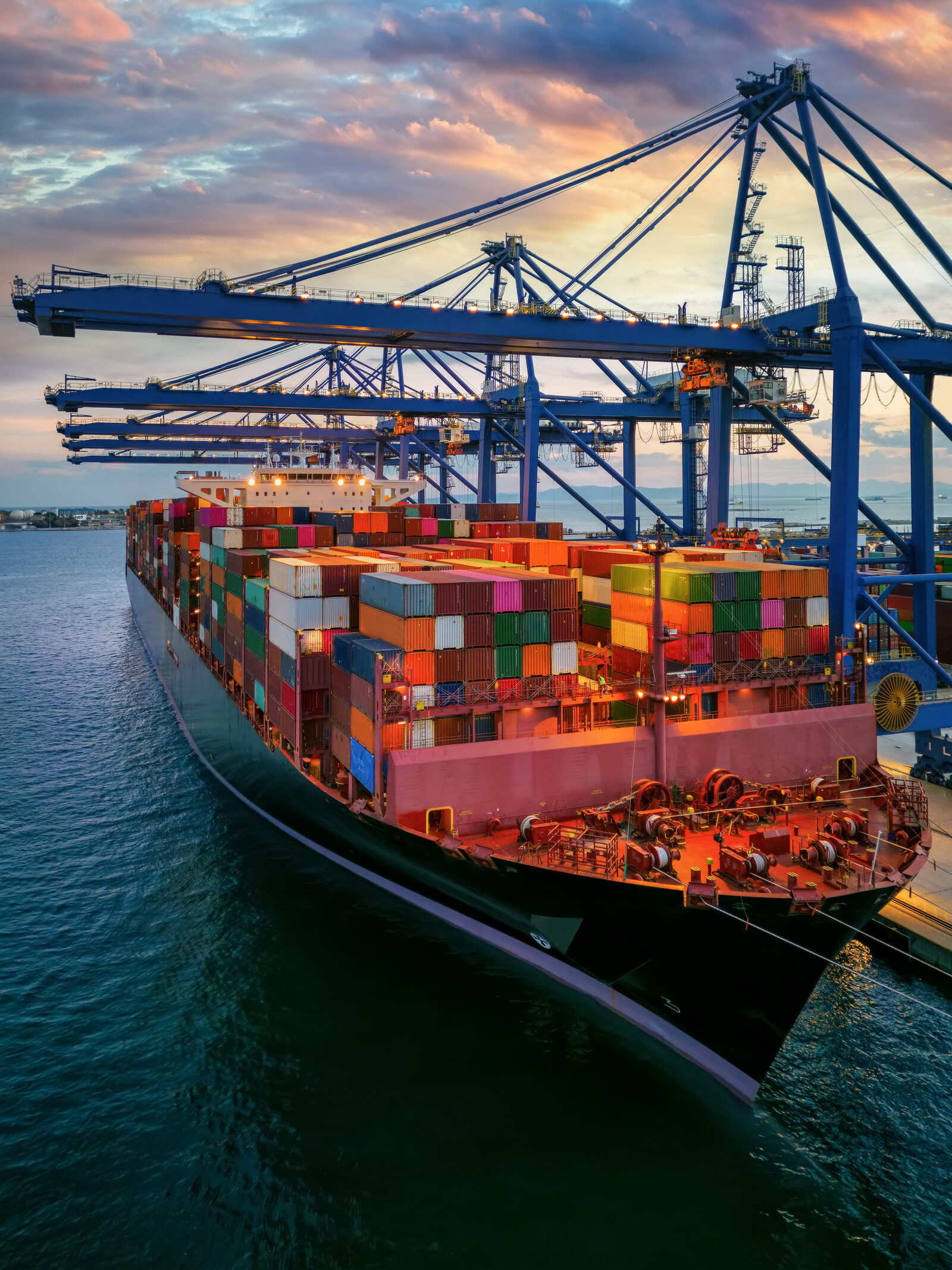 Container vessel berthed under ship-to-shore cranes at dusk
