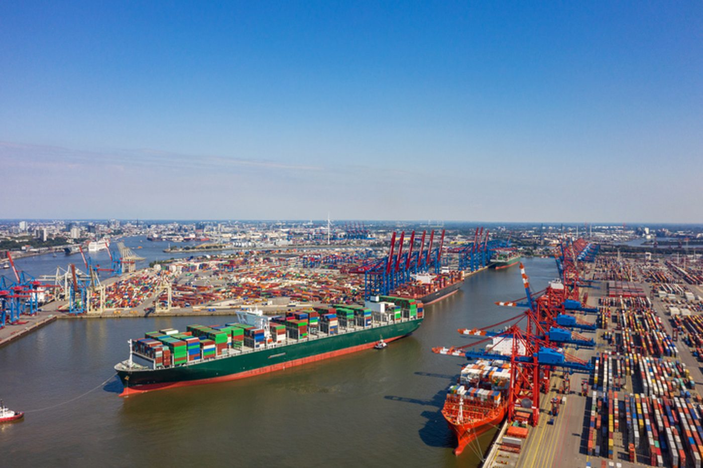 Aerial view of a container vessel being worked through a narrow channel between busy terminal berths