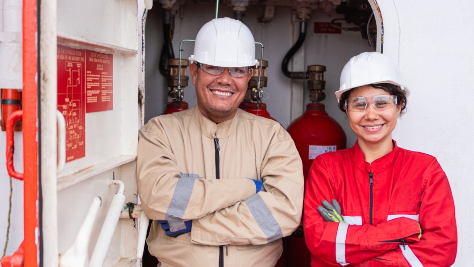 Two smiling seafarers in coveralls and hard hats aboard ship